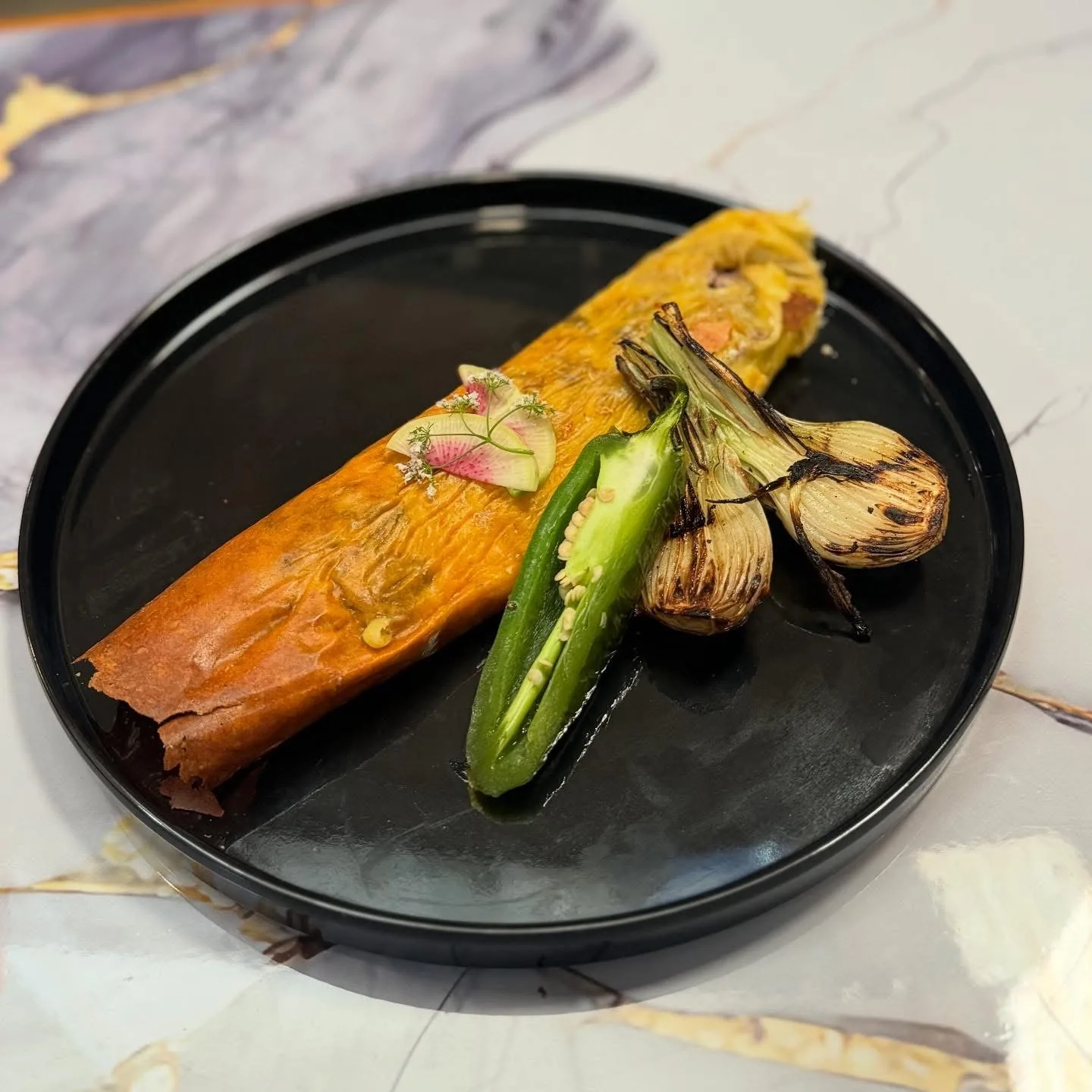 Platillo dorado servido en plato negro